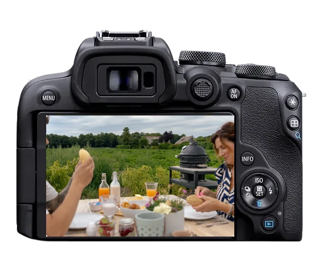 Camera met een bedrijfsfoto van een buitenontbijt bij B&B De Gouden Ploeg: gasten aan een gedekte tafel met een kamado-barbecue voor een groene akker